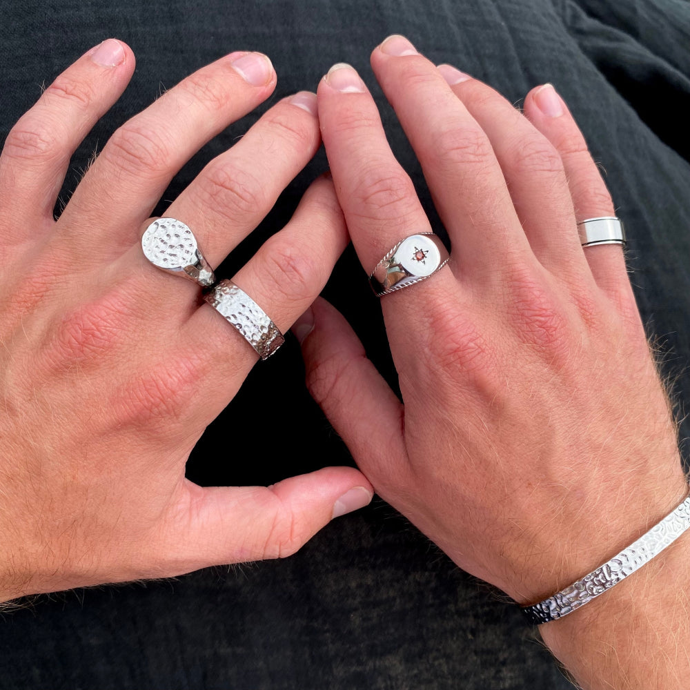 Close-up of two hands wearing silver rings on a dark background