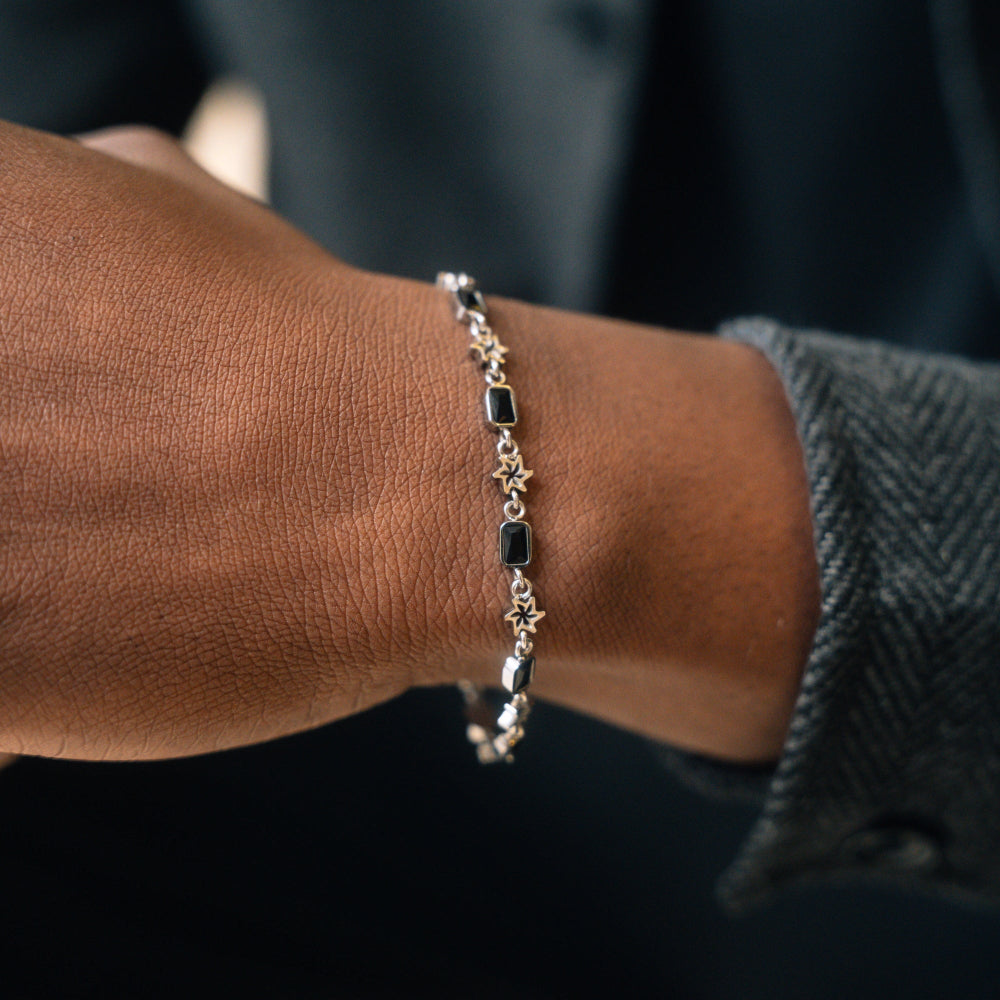 Close-up of a wrist wearing a gold bracelet with black stones against a dark background