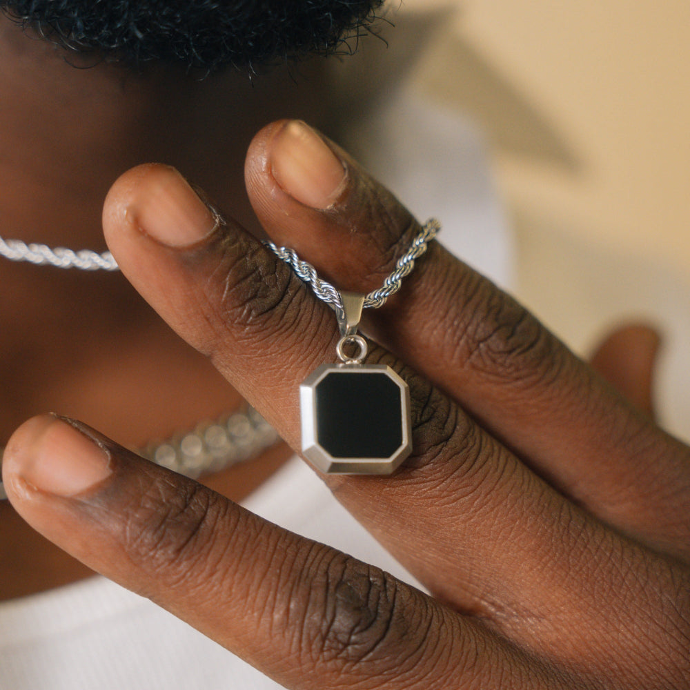 Hand wearing a silver ring with a black pendant on a neutral background