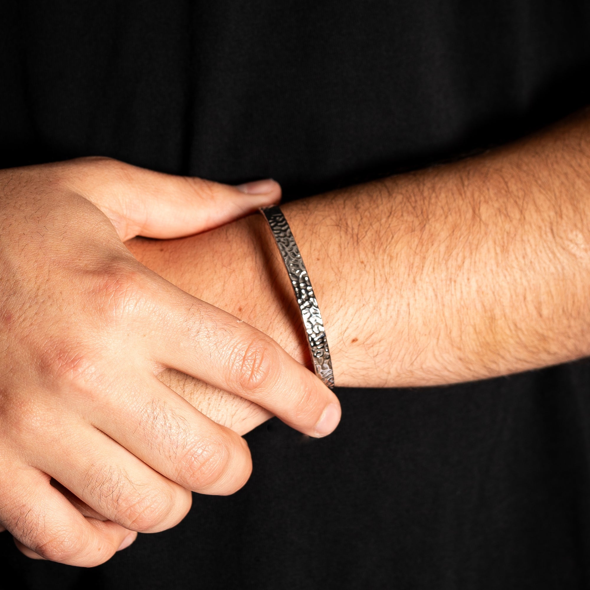 Close-up of a hand adjusting a silver bracelet on an arm against a black background