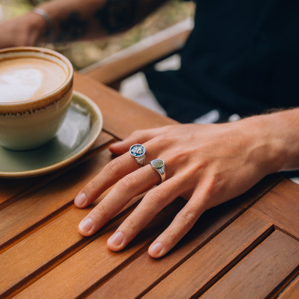 Hand with rings on a wooden table next to a cup of coffee