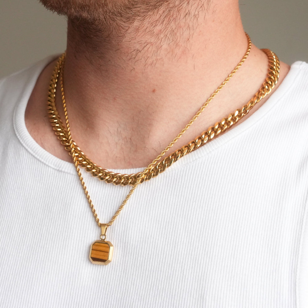 Close-up of a person wearing two gold chain necklaces with a plain background