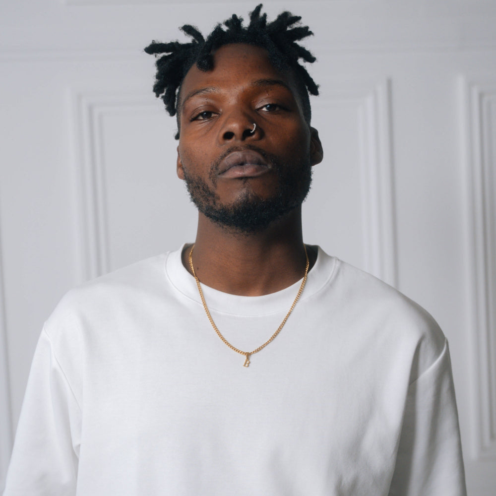 Man wearing a white sweatshirt and gold necklace against a plain background