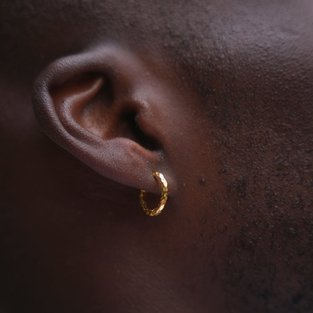 Gold hoop earring on a person's ear with dark skin background