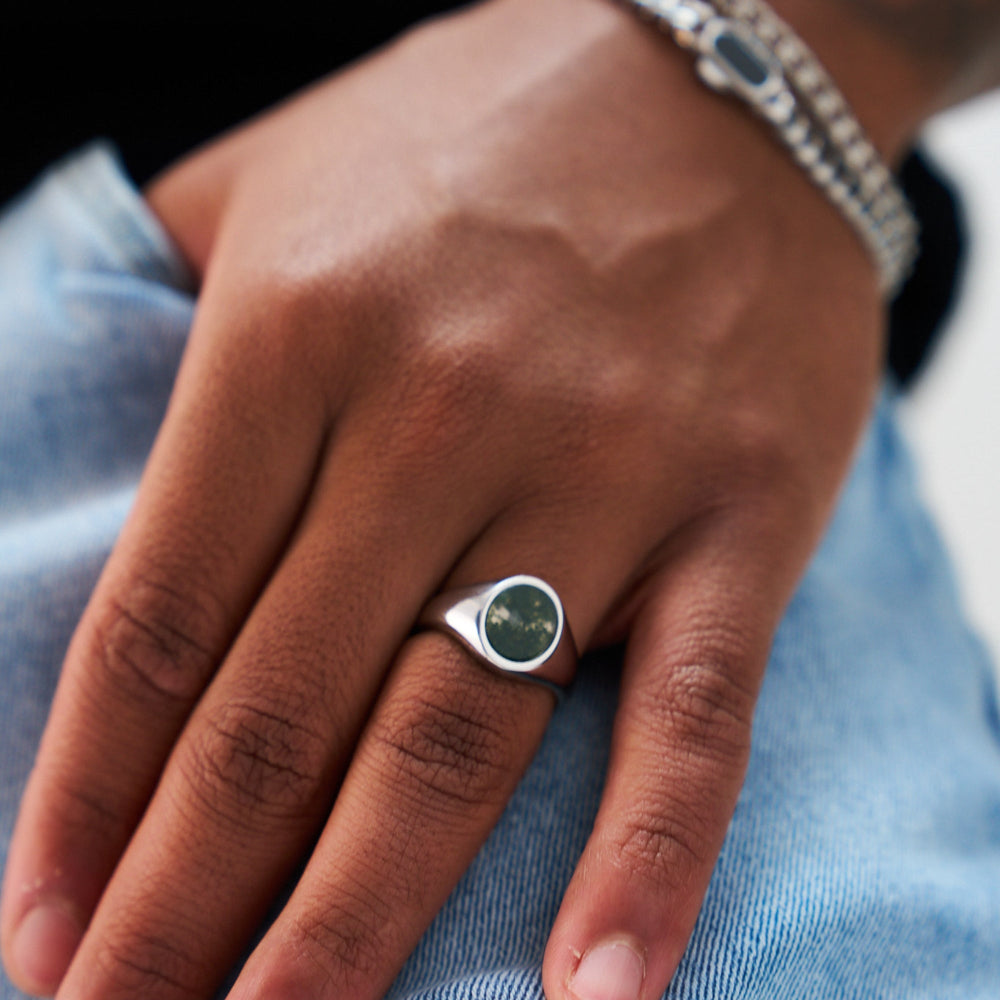 Hand wearing a silver ring with a green stone on a blurred background