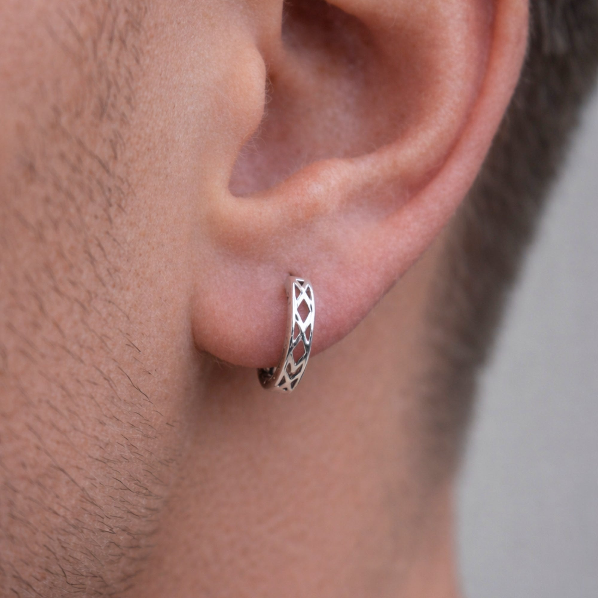 Close-up of a man wearing a silver hoop earring with a geometric design.
