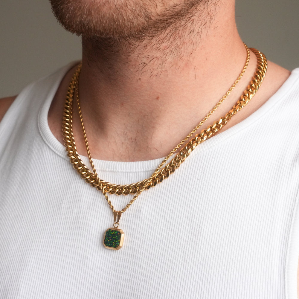 Gold chain necklace with a green pendant on a person wearing a white tank top.