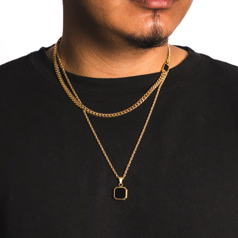 Man wearing a gold chain necklace with a square pendant on a black shirt.