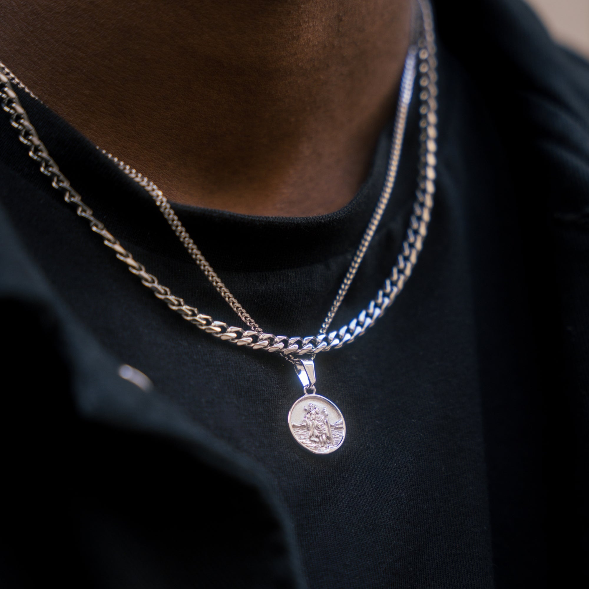 Close-up of a person wearing two necklaces with a pendant on a dark background
