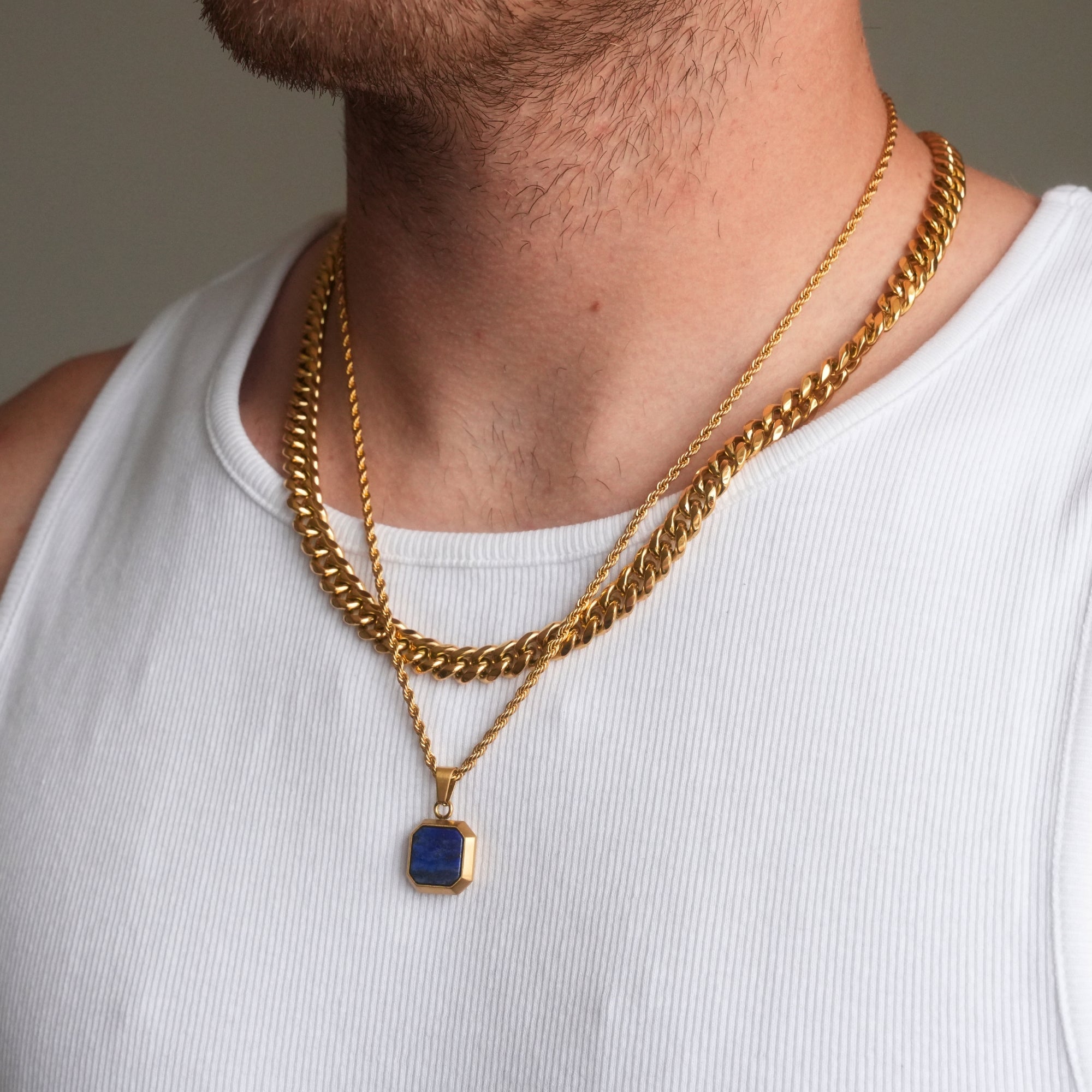 Gold chain necklace with a blue pendant worn by a person in a white tank top.