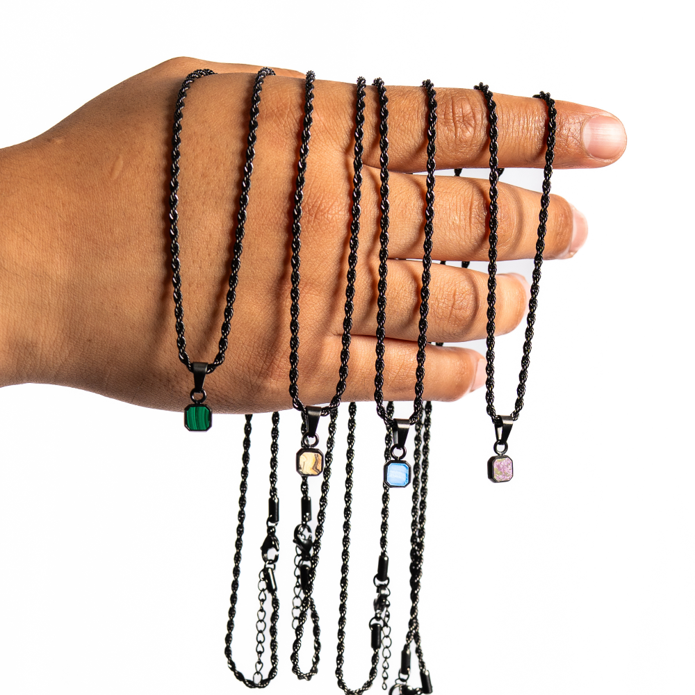 Hand wearing multiple black necklaces with various colored pendants on a white background