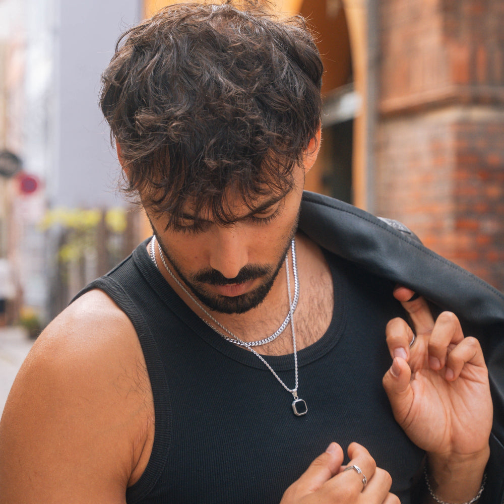 Man wearing a black tank top and jacket with a blurred urban background