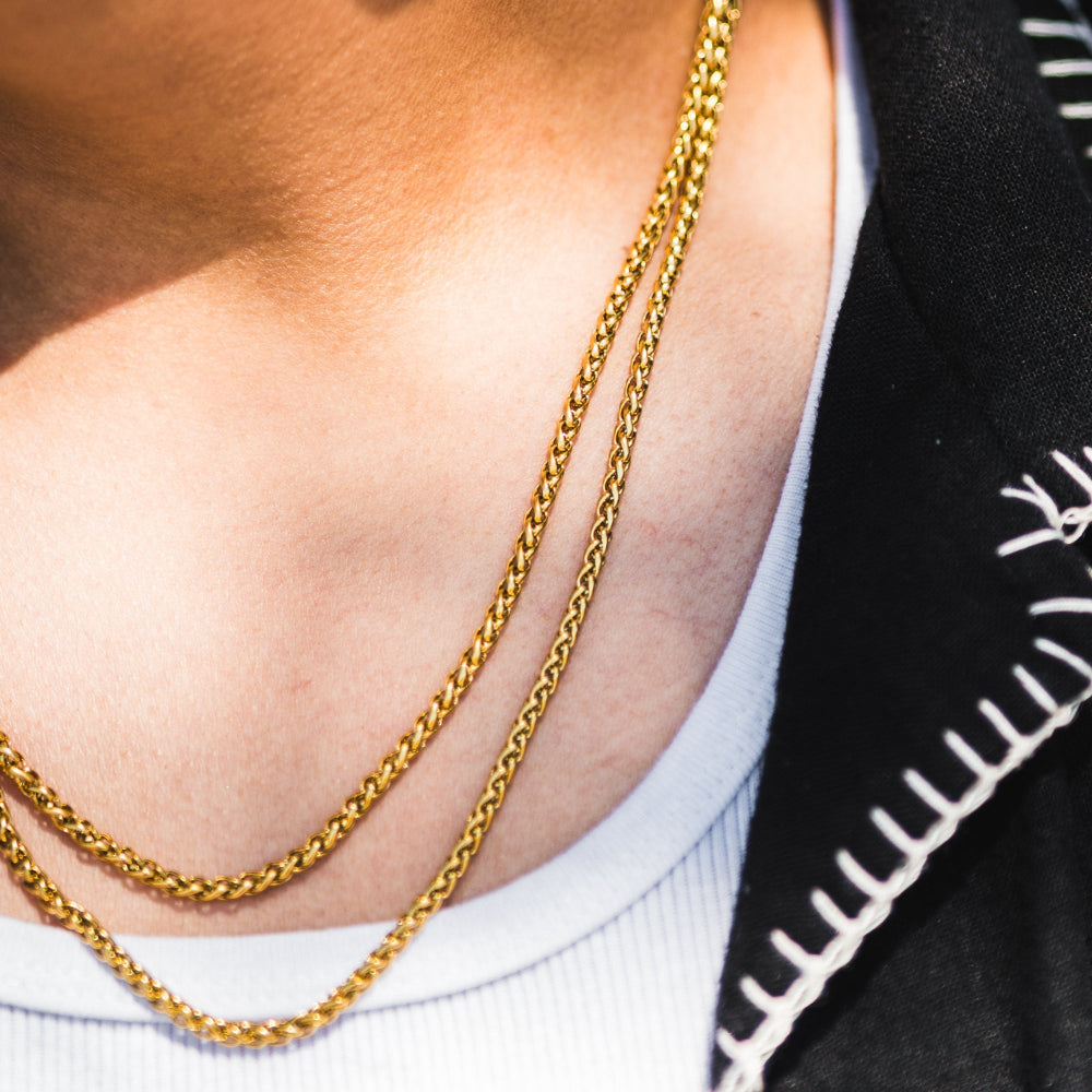 Gold chain necklace on a person wearing a white top with black sleeves.