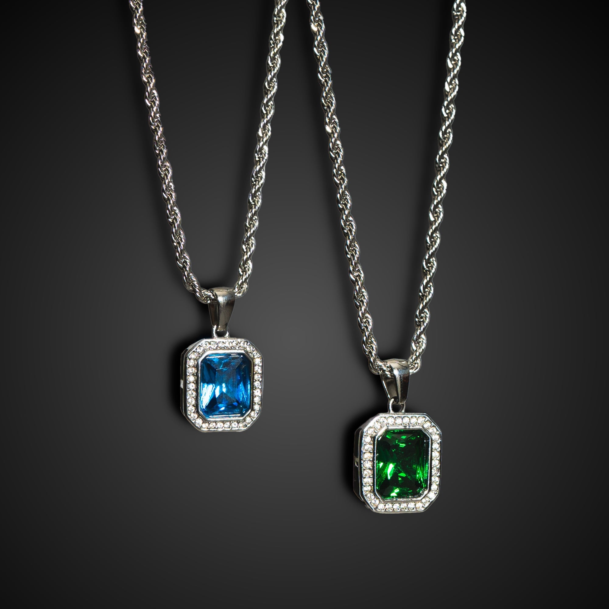Two silver pendants with blue and green gemstones on a dark background