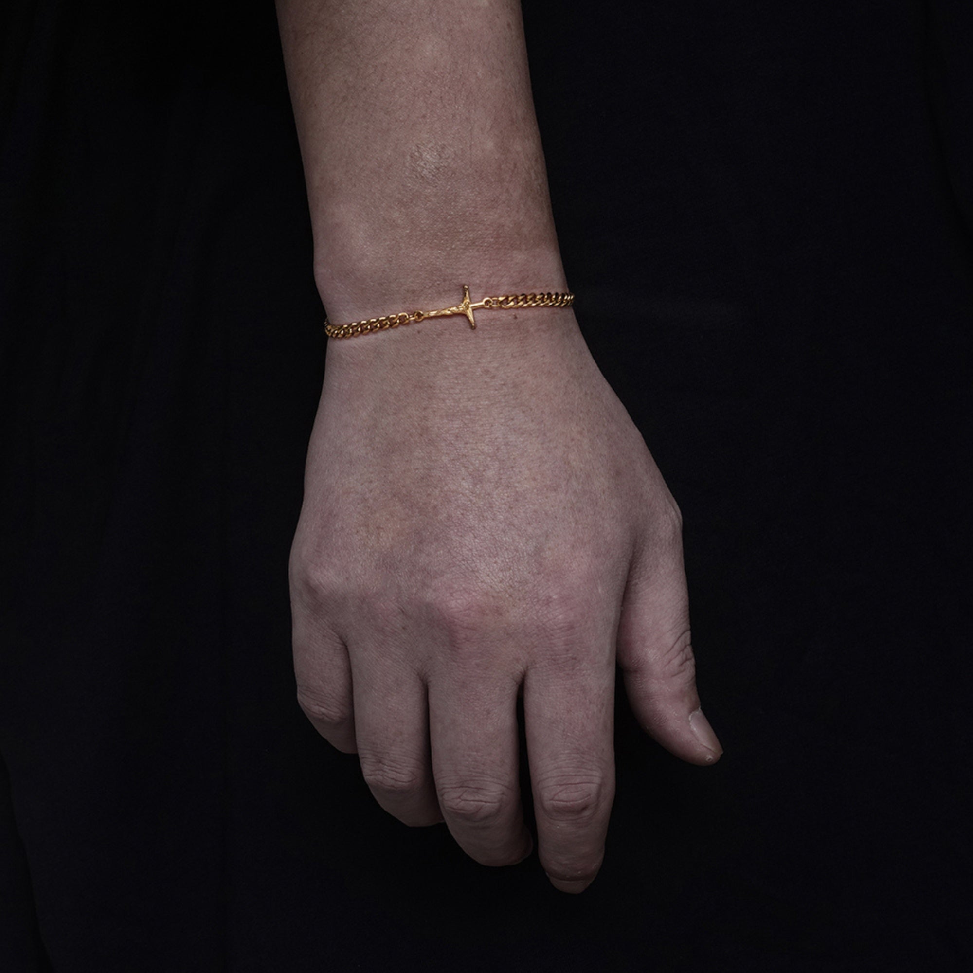 Hand wearing a gold bracelet on a black background