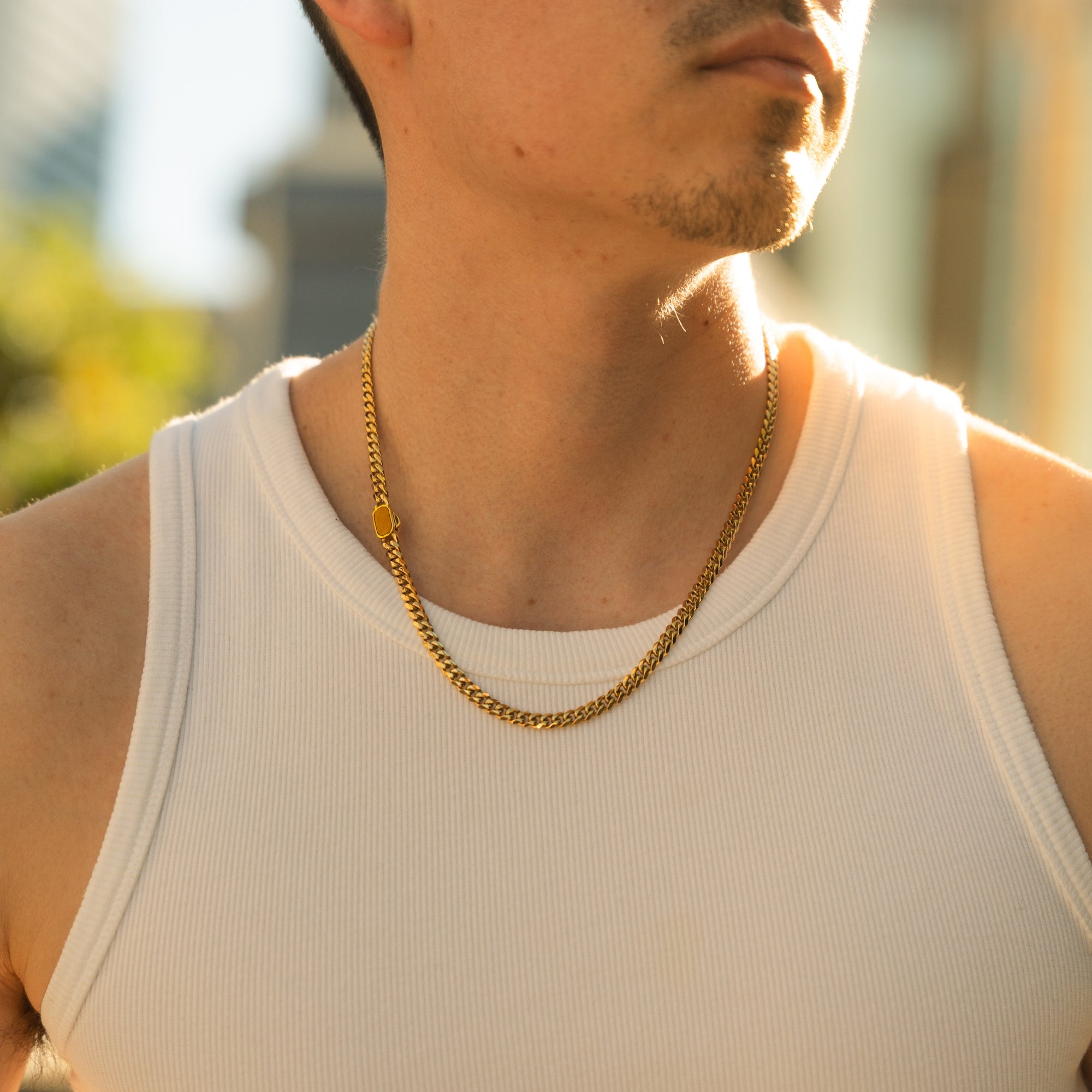 Man wearing a gold chain necklace and white tank top outdoors