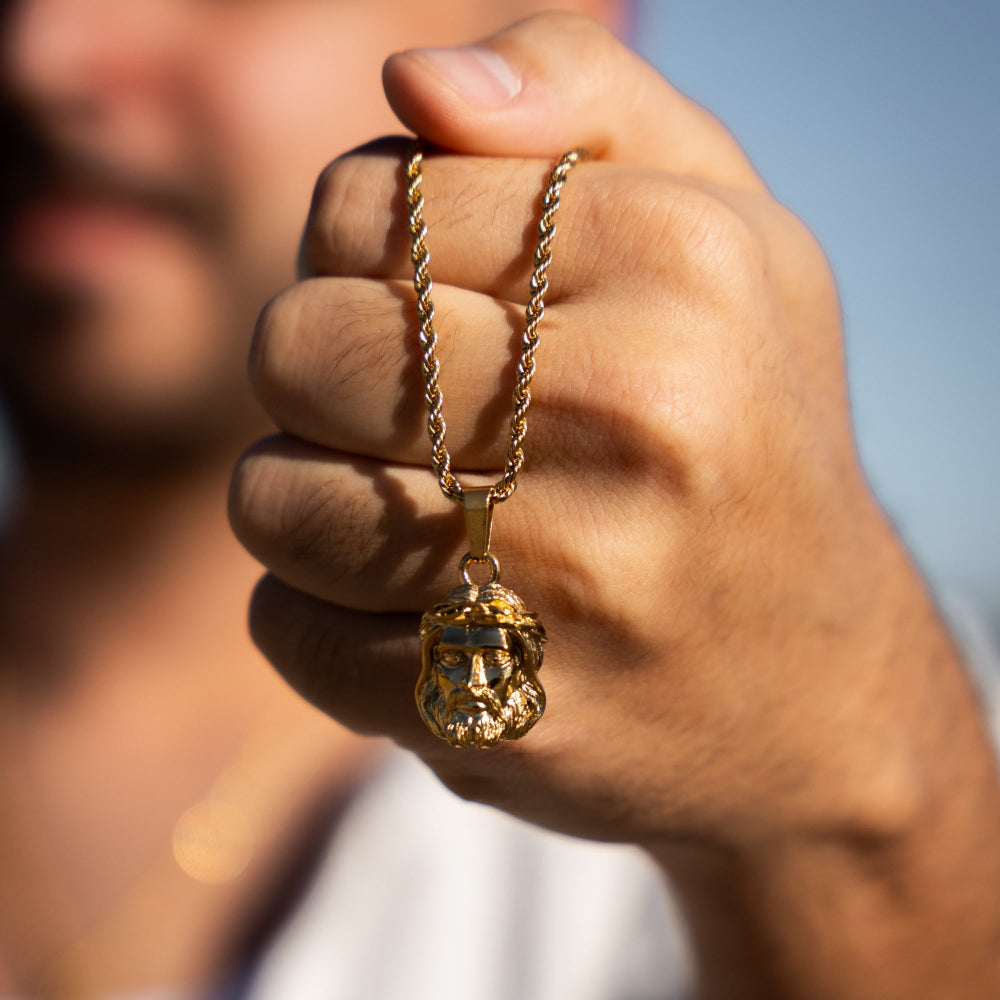 Hand holding a gold necklace with a pendant against a blurred background