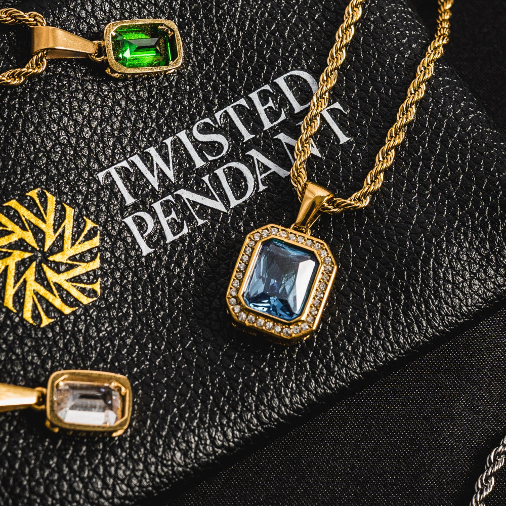 Gold pendant with blue gemstone on a black textured surface with 'Twisted Pendant' branding.