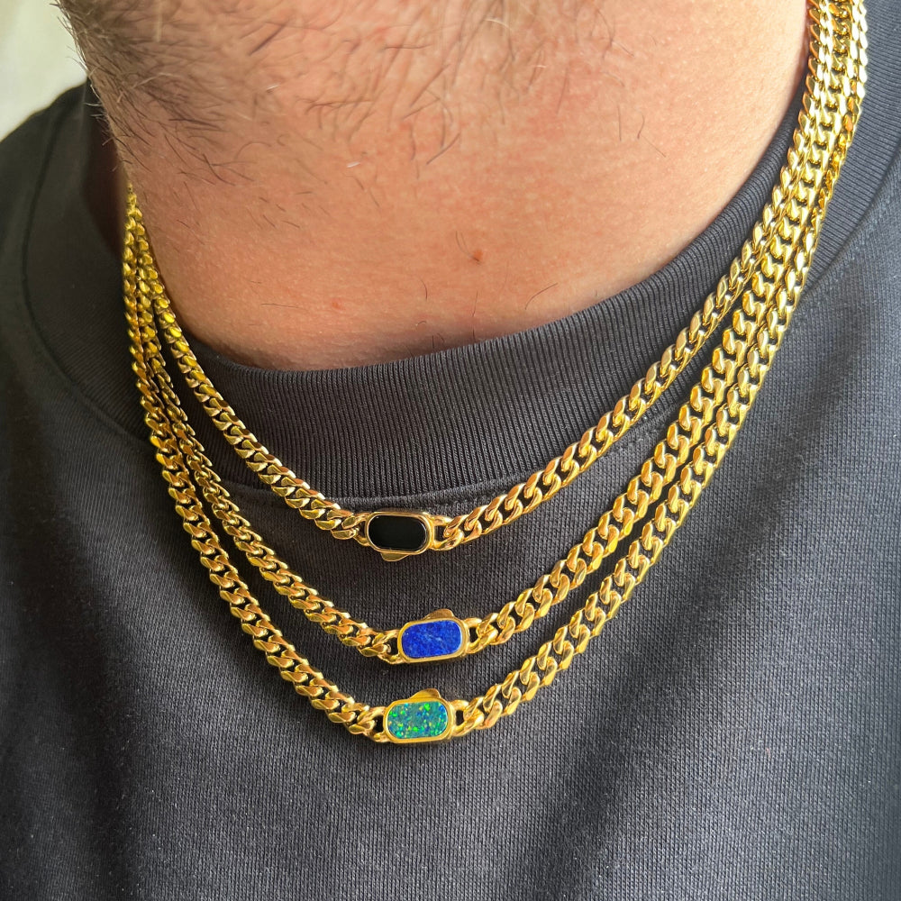 Three gold chain necklaces with colored pendants on a person wearing a dark shirt.