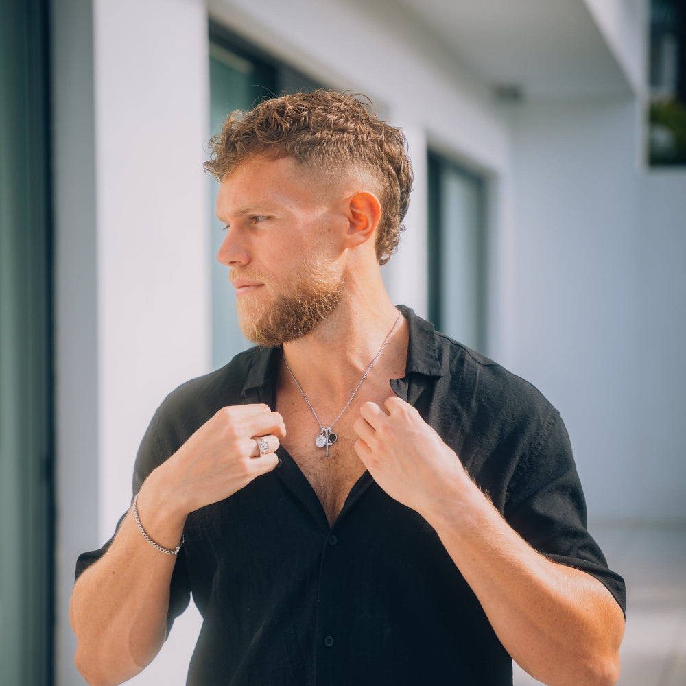 Man adjusting his black shirt outdoors with a blurred background