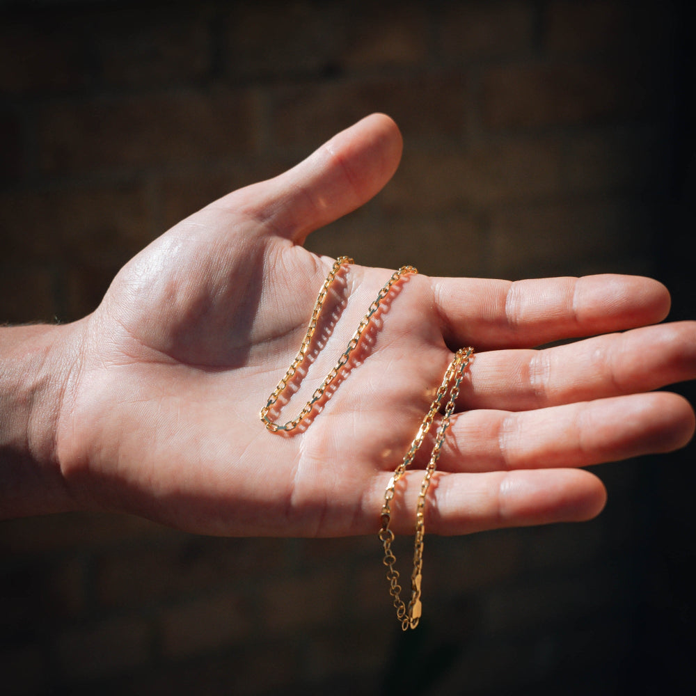 Hand holding two gold chains against a dark background