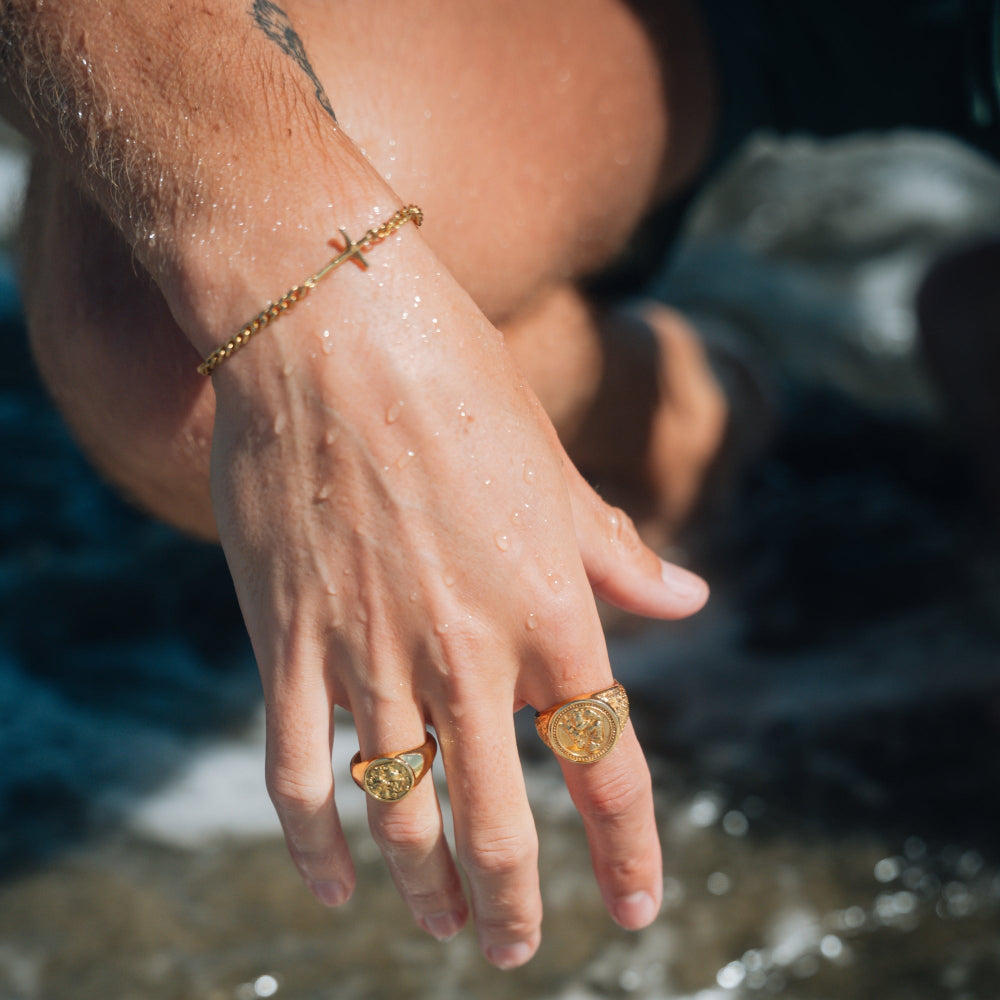 Hand with gold rings and bracelet near water