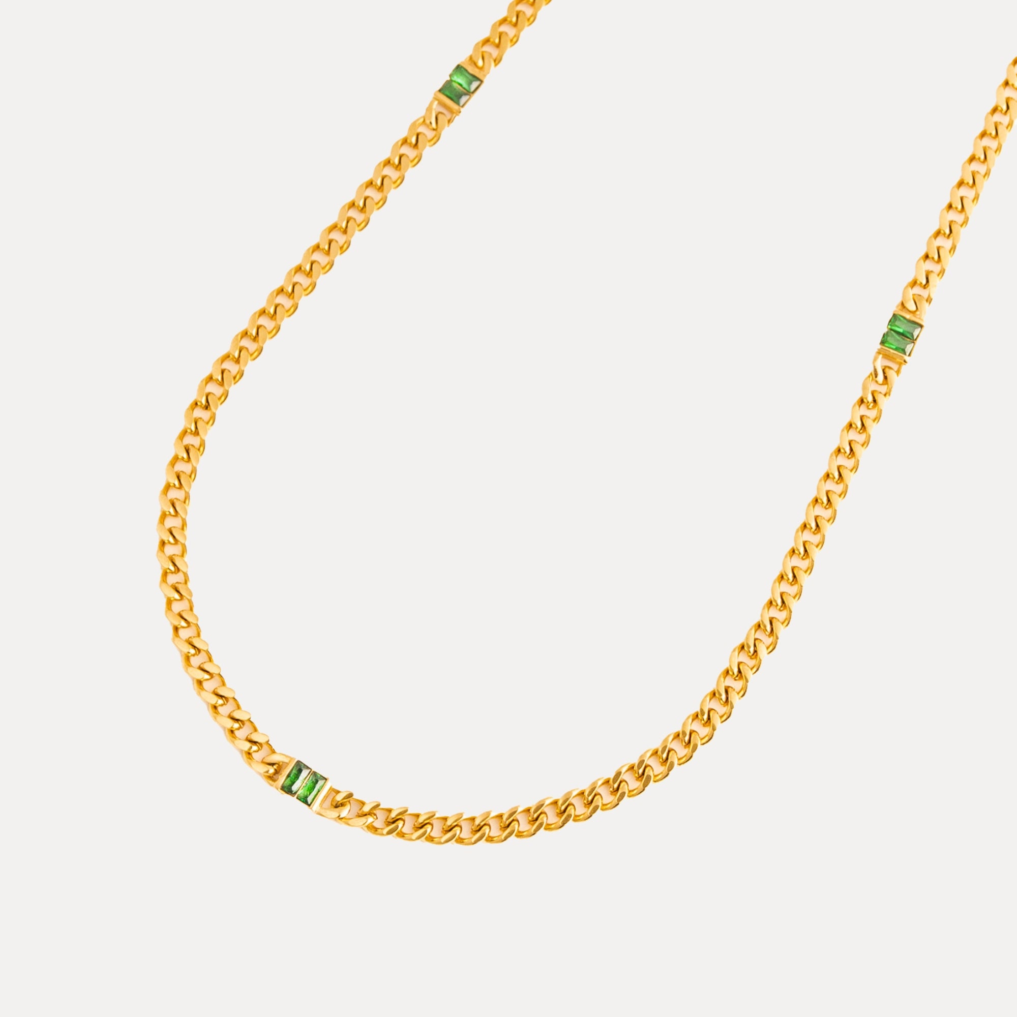 Gold chain necklace with green gemstones on a light gray background