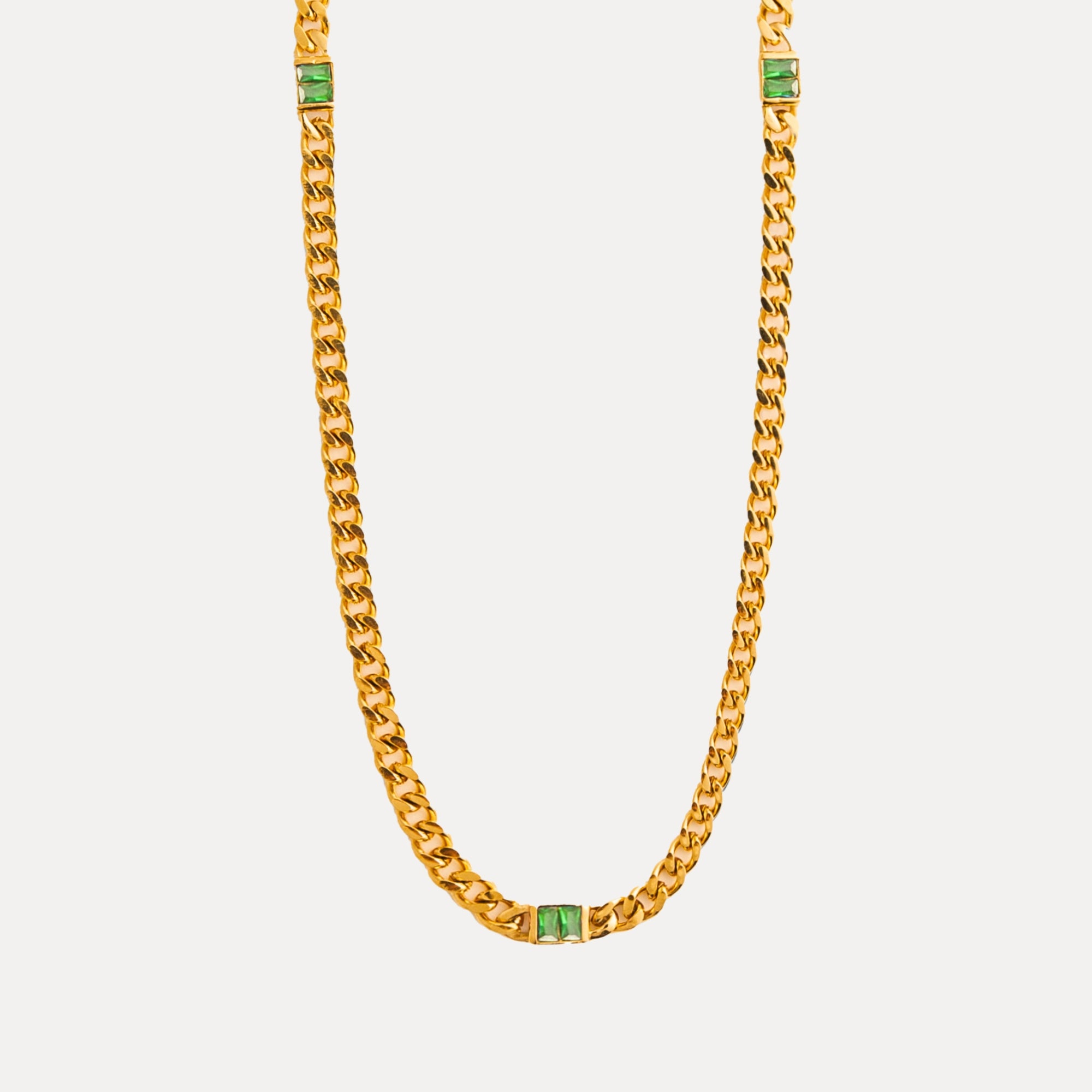Gold chain necklace with green gemstones on a light gray background