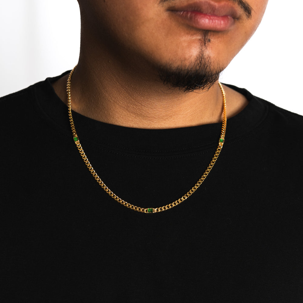 Man wearing a gold chain necklace with colored beads on a plain background