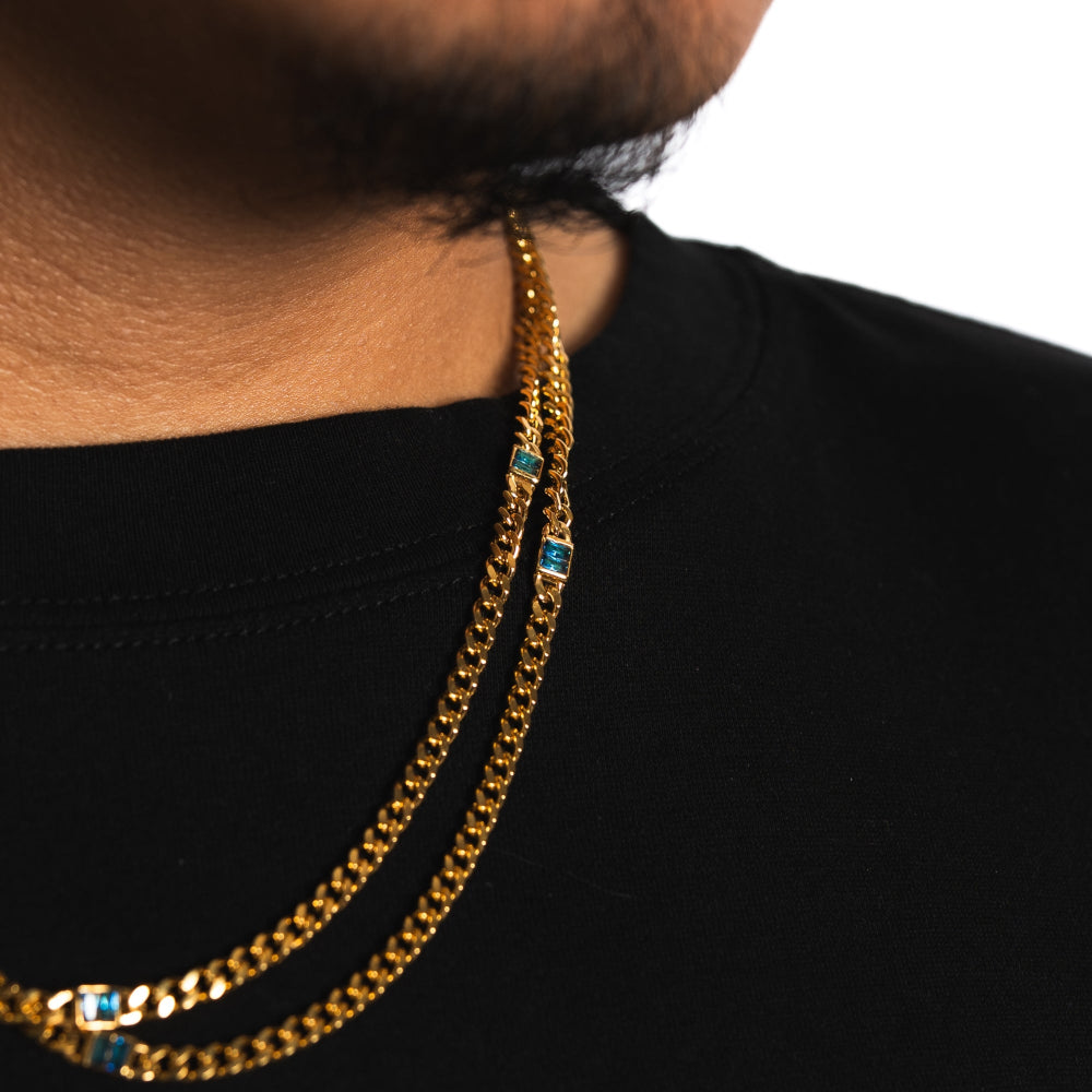 Gold chain necklace with blue stones worn by a person on a black background