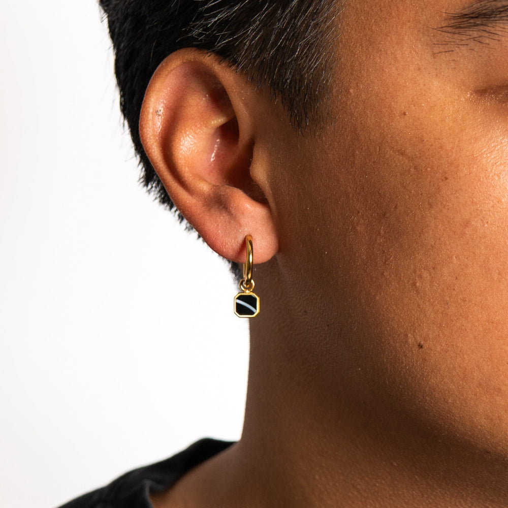 Gold earring with a black and gold stone worn by a person on a white background