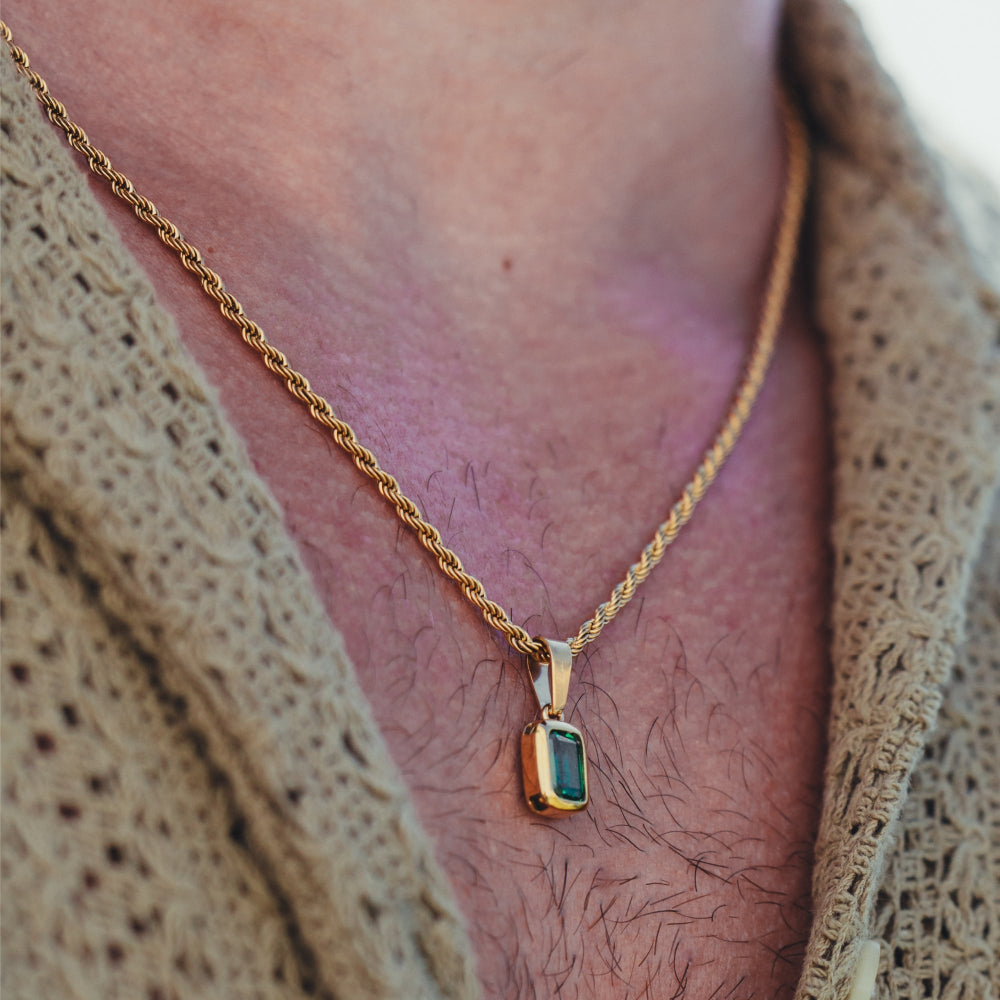 Gold necklace with a green gemstone pendant on a person wearing a beige cardigan.