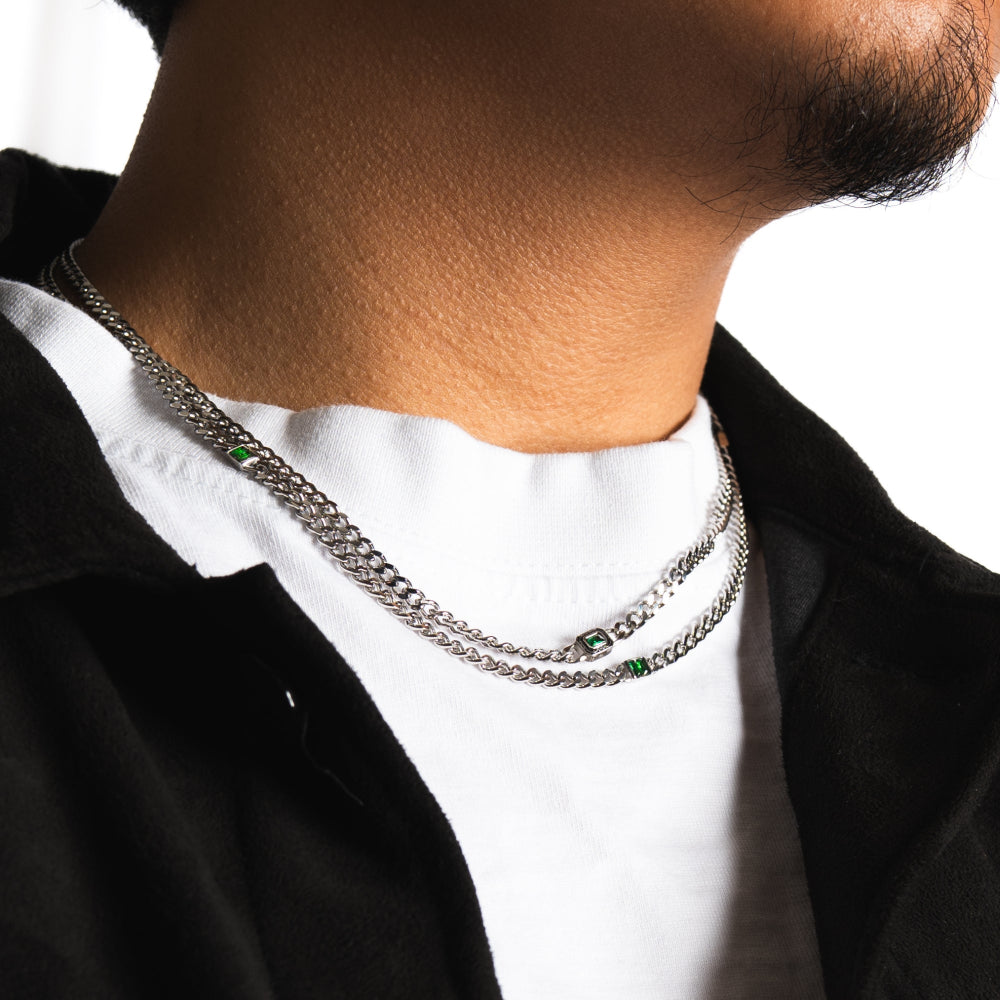 Person wearing a silver chain necklace with green stones on a white background