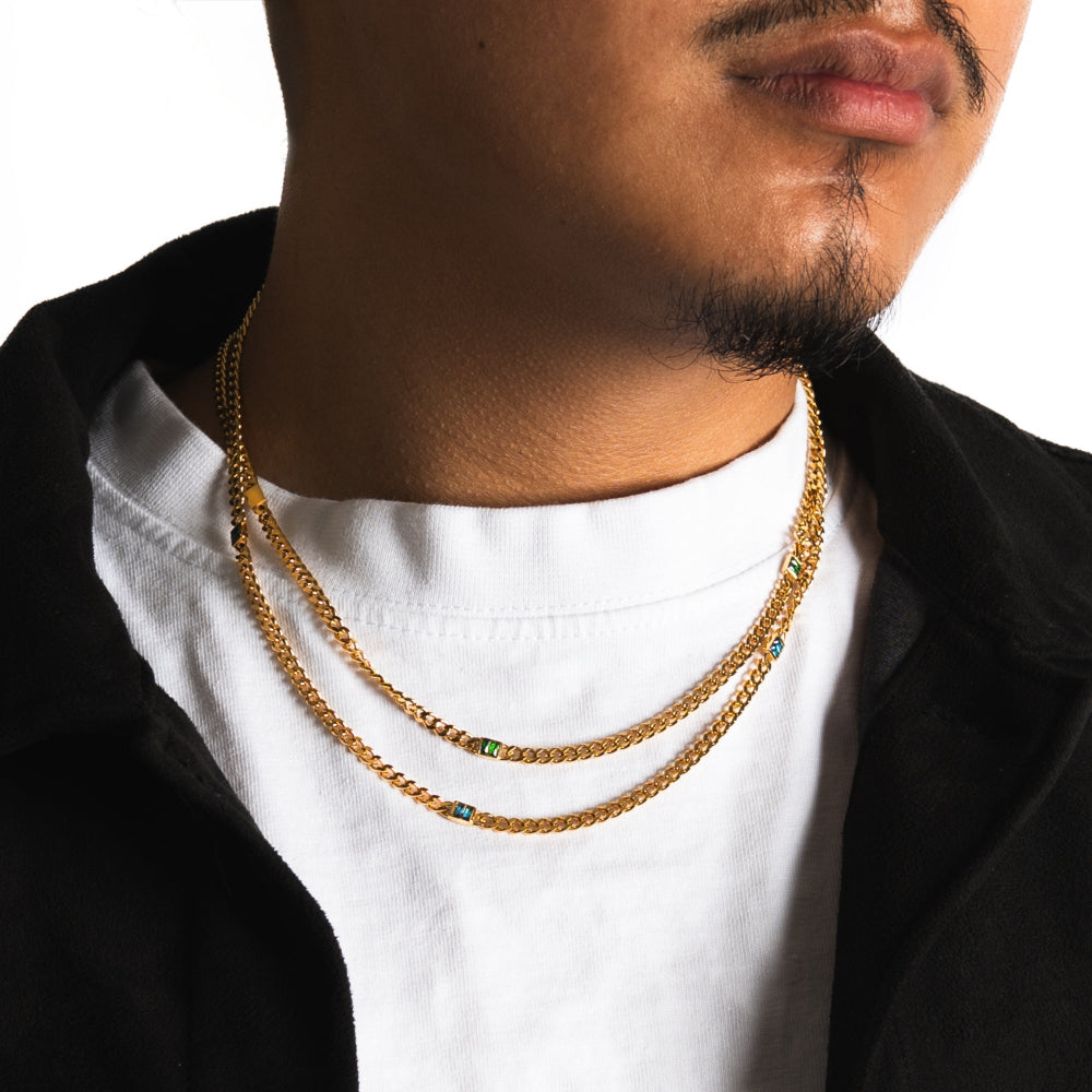 Man wearing a white shirt and black jacket with gold chains around his neck.
