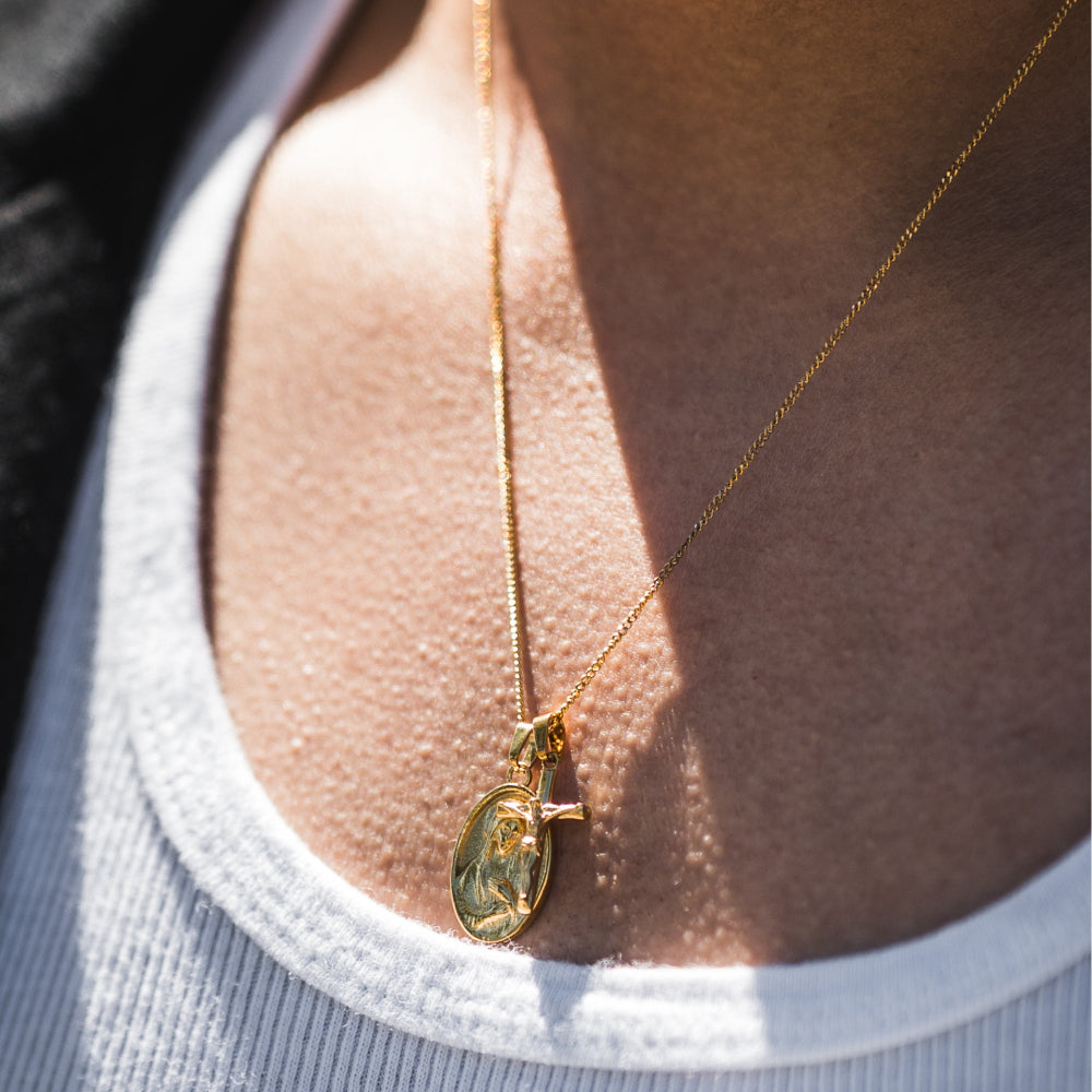 Gold necklace with a pendant on a person wearing a light gray top.