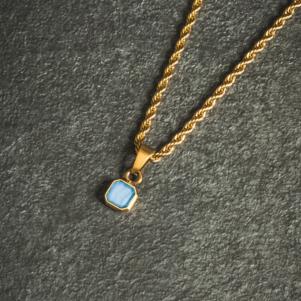 Gold necklace with a blue pendant on a dark gray surface
