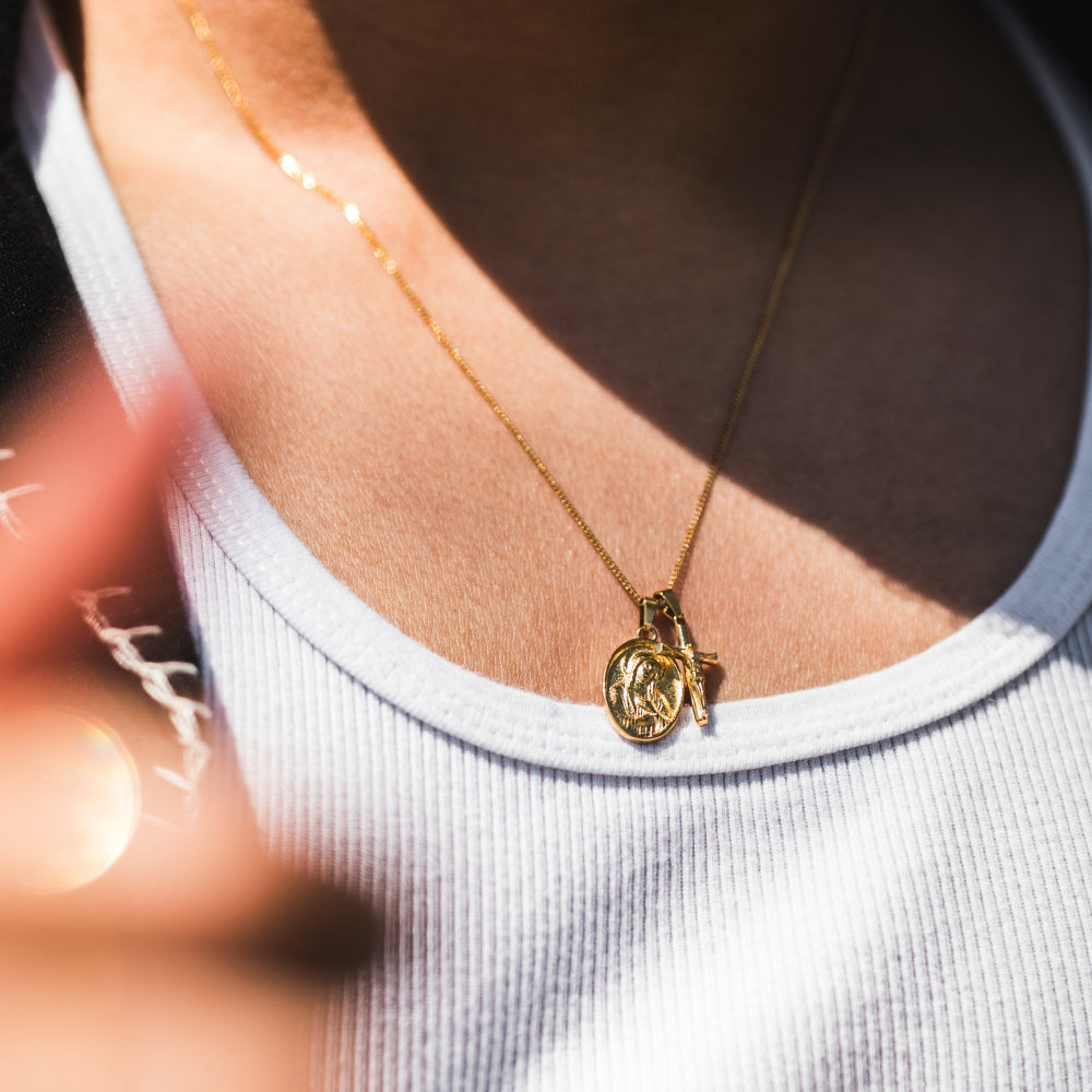 Gold necklace with a pendant on a person wearing a white tank top.