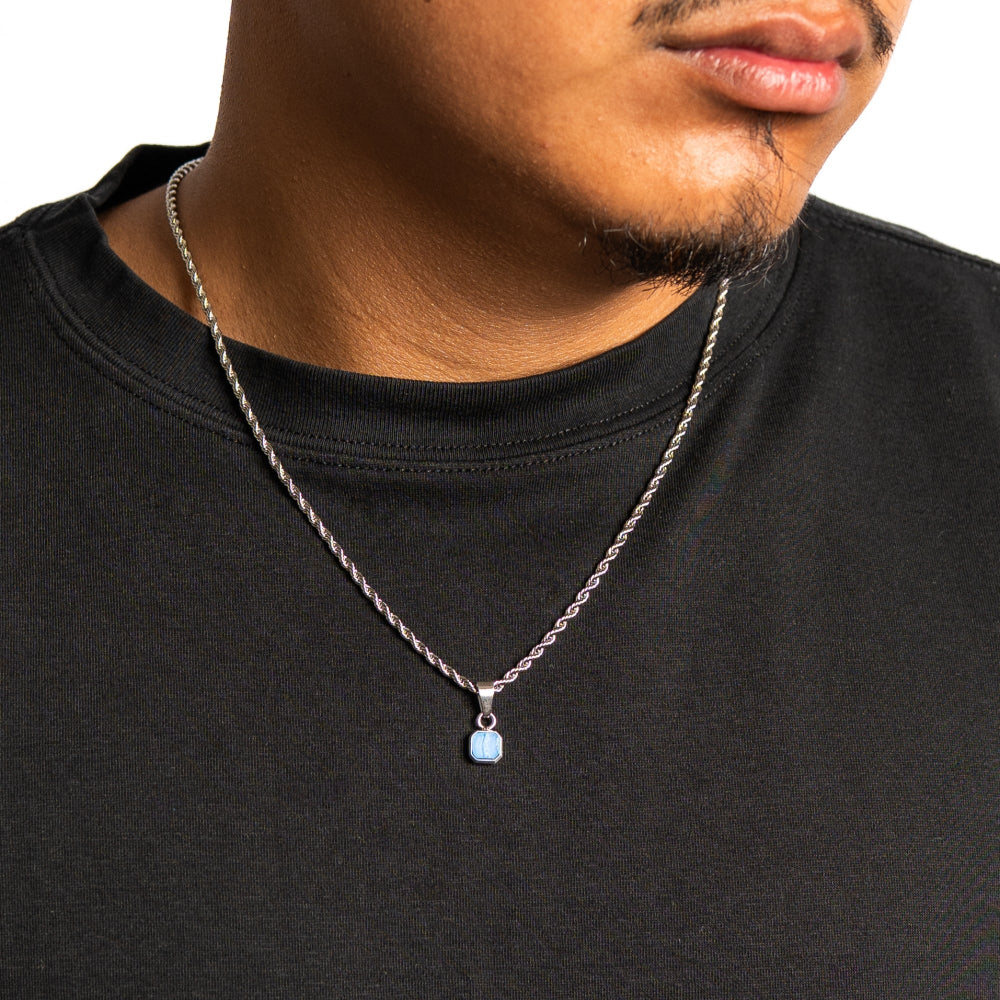 Man wearing a black shirt with a silver necklace featuring a blue pendant.