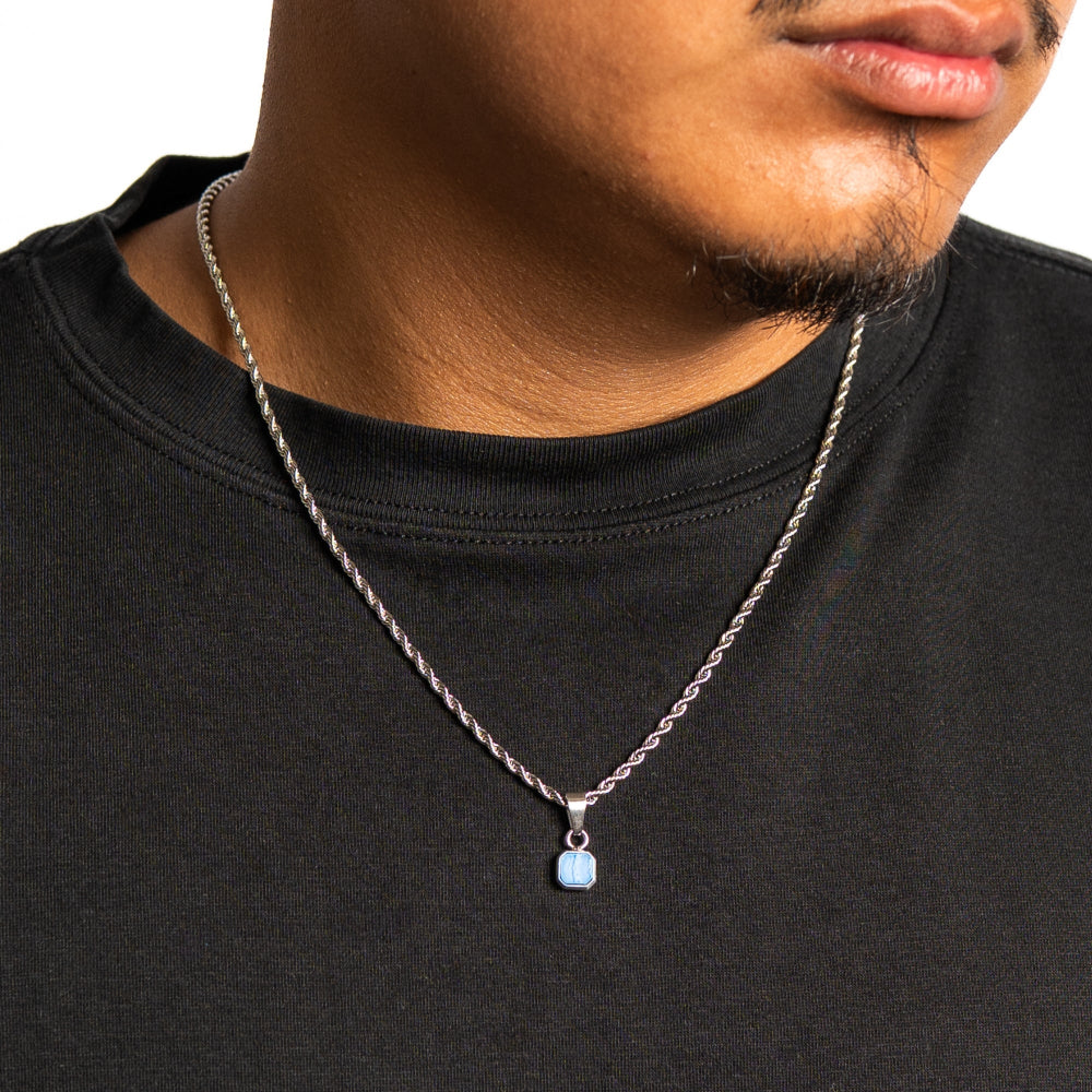 Man wearing a black shirt with a silver necklace featuring a blue pendant.
