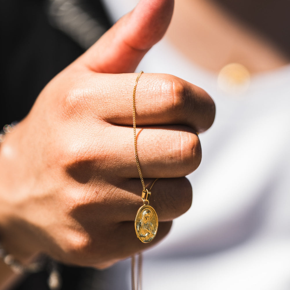 Gold necklace with pendant held in a hand against a blurred background