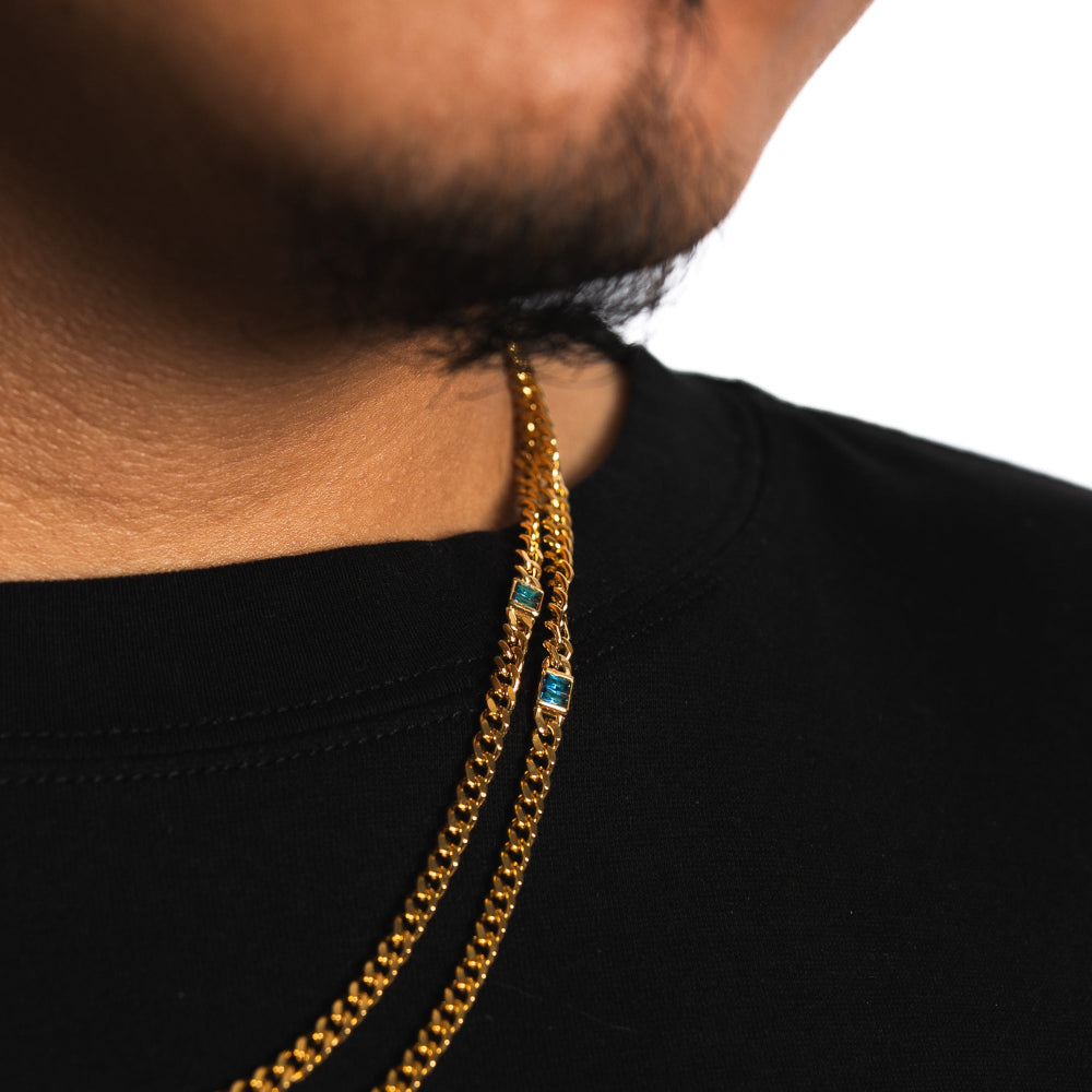 Close-up of a person wearing a gold chain necklace with blue stones on a black background