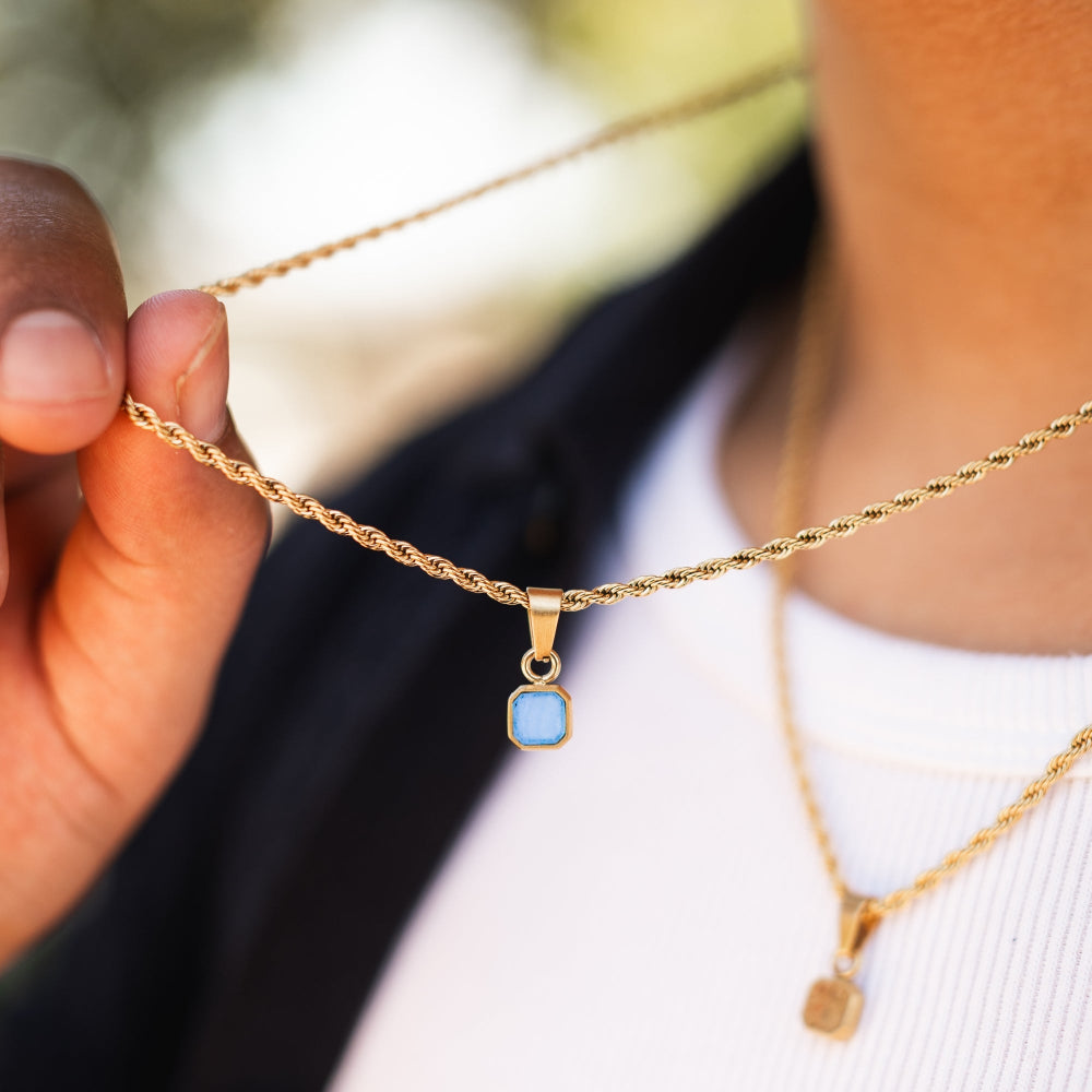 Gold necklace with a blue pendant held by a hand