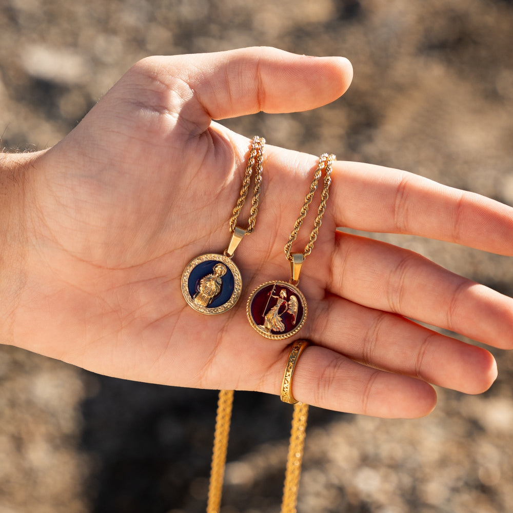Hand holding two gold necklaces with circular pendants against a blurred natural background