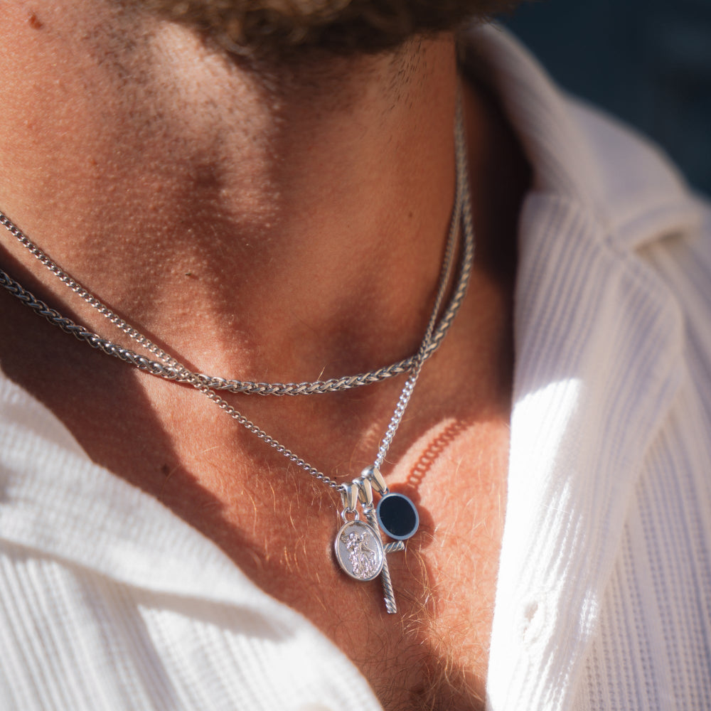 Close-up of a person wearing multiple silver necklaces with pendants.