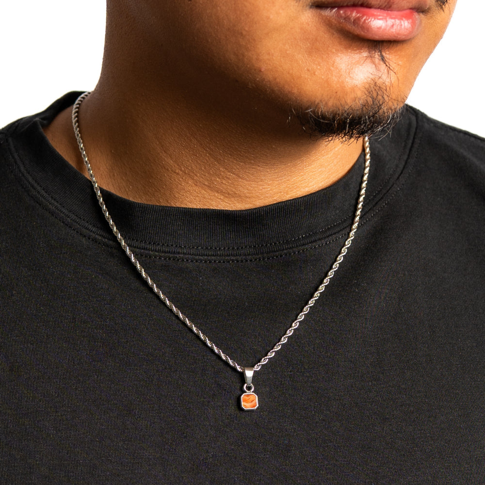 Man wearing a black shirt with a silver chain necklace featuring a small pendant.