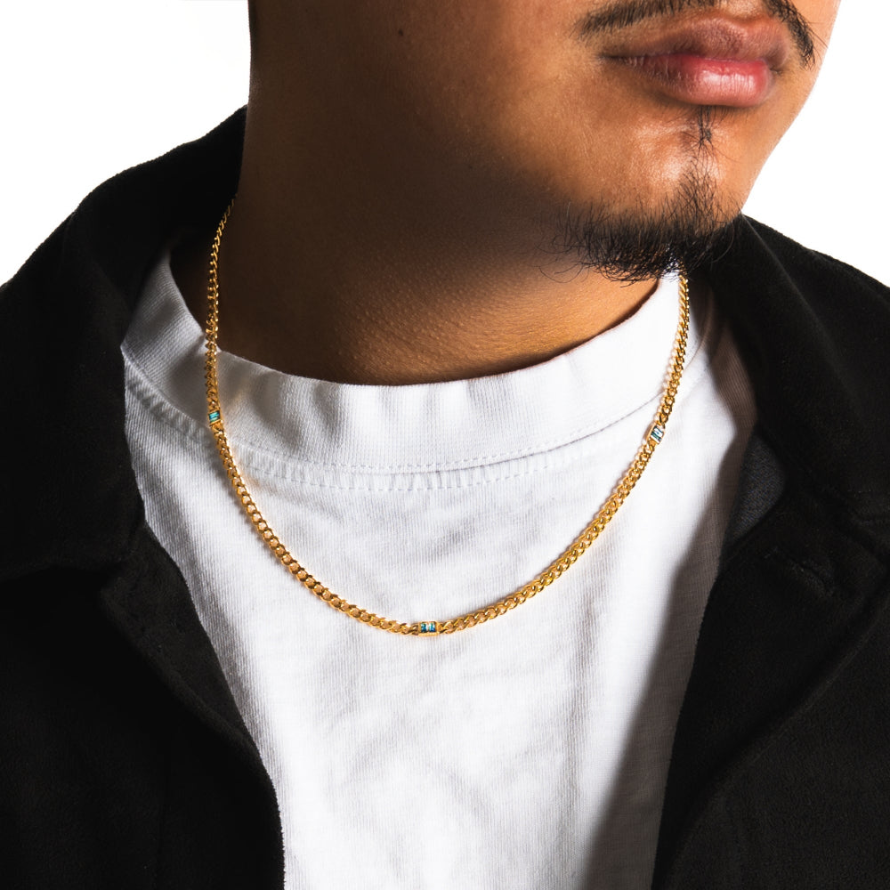 Man wearing a gold chain necklace with a white shirt and black jacket.