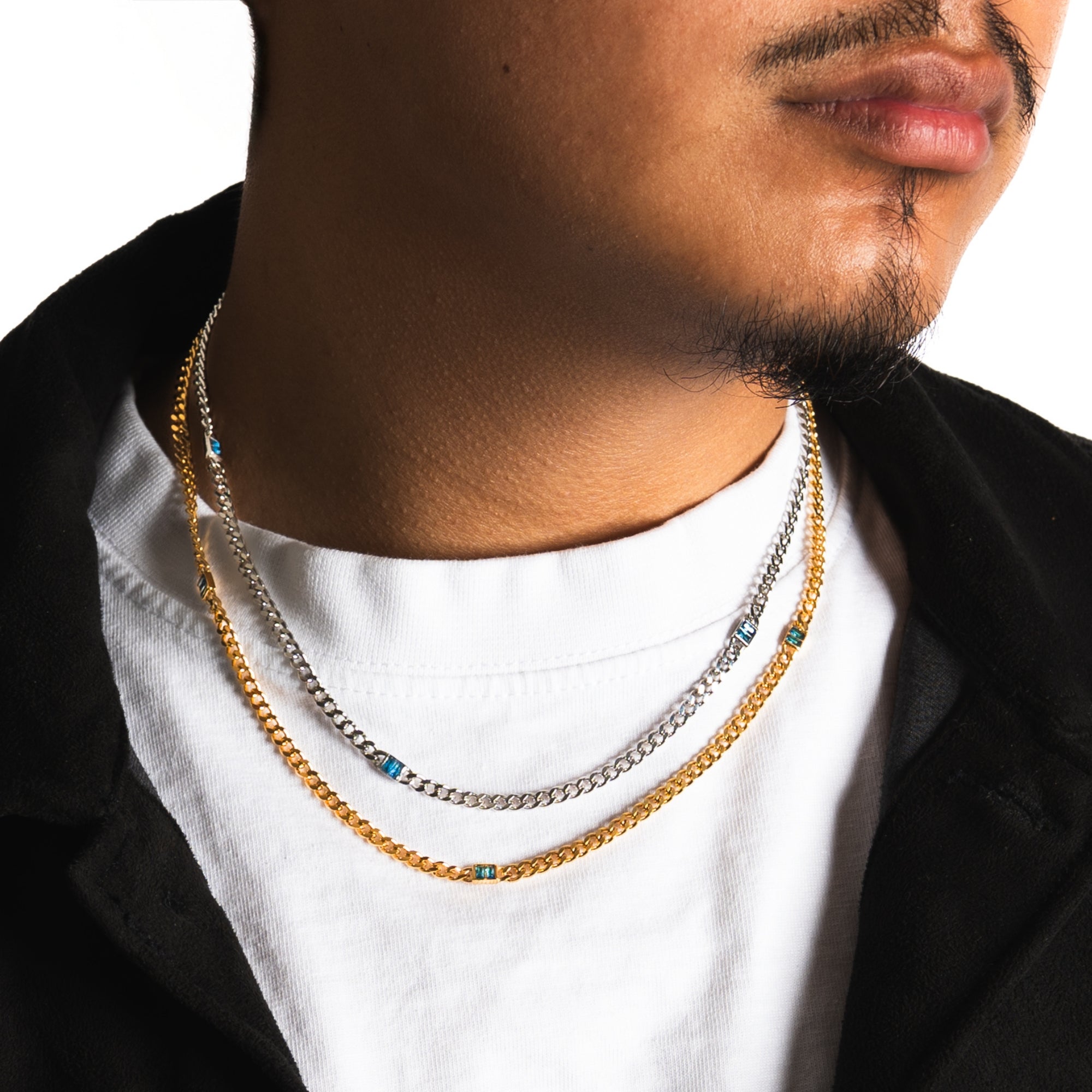 Person wearing multiple necklaces with a white shirt and black jacket