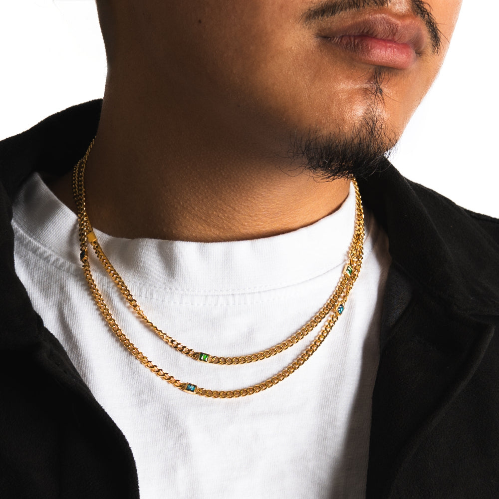 Man wearing a gold chain necklace with a white shirt and black jacket.