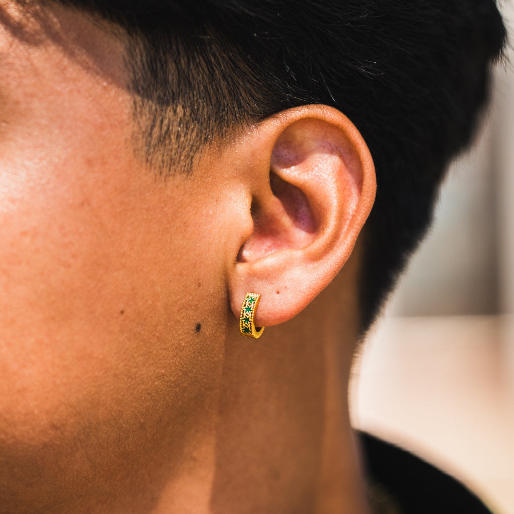 Close-up of an ear wearing a gold hoop earring with green gemstones.