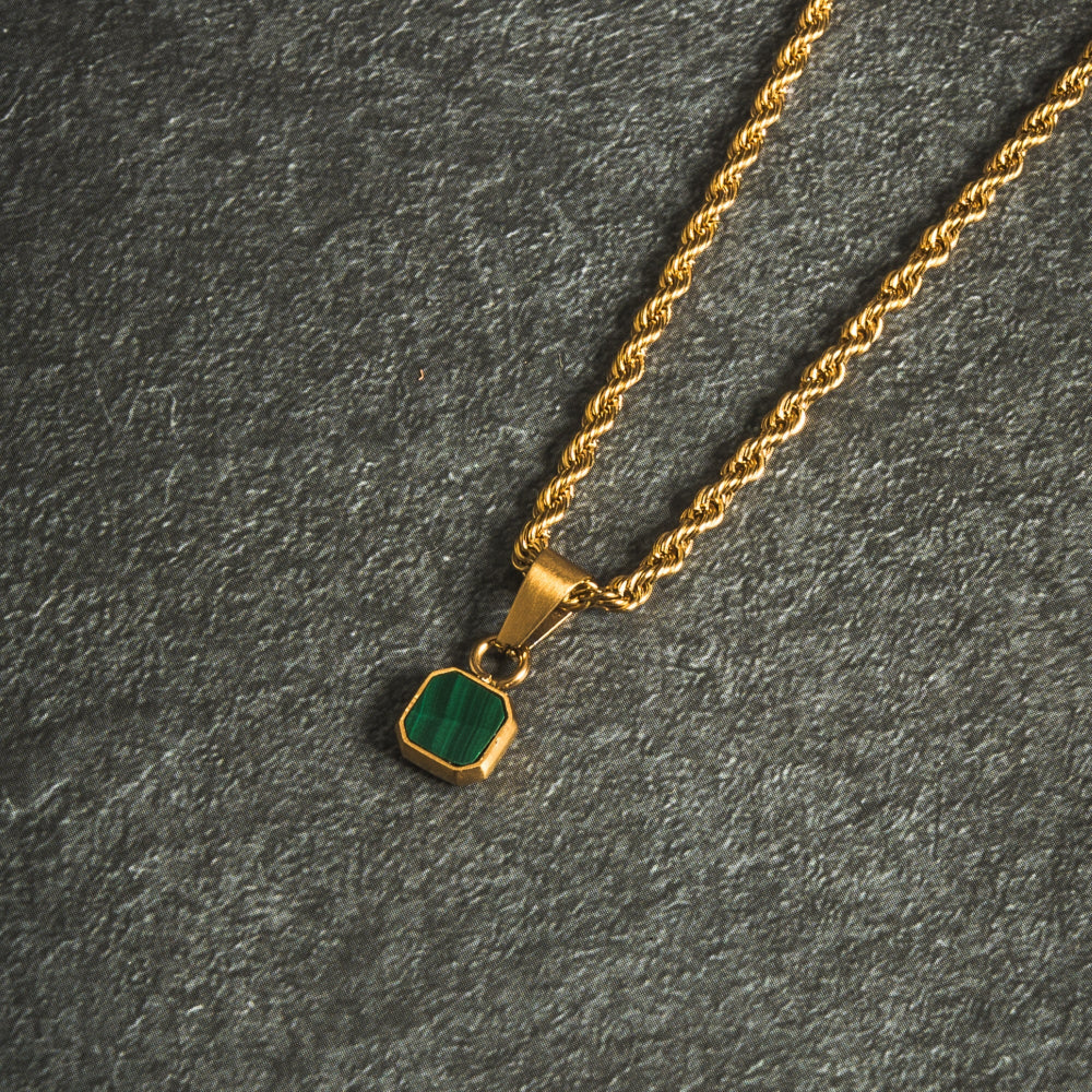Gold necklace with a green pendant on a dark gray background